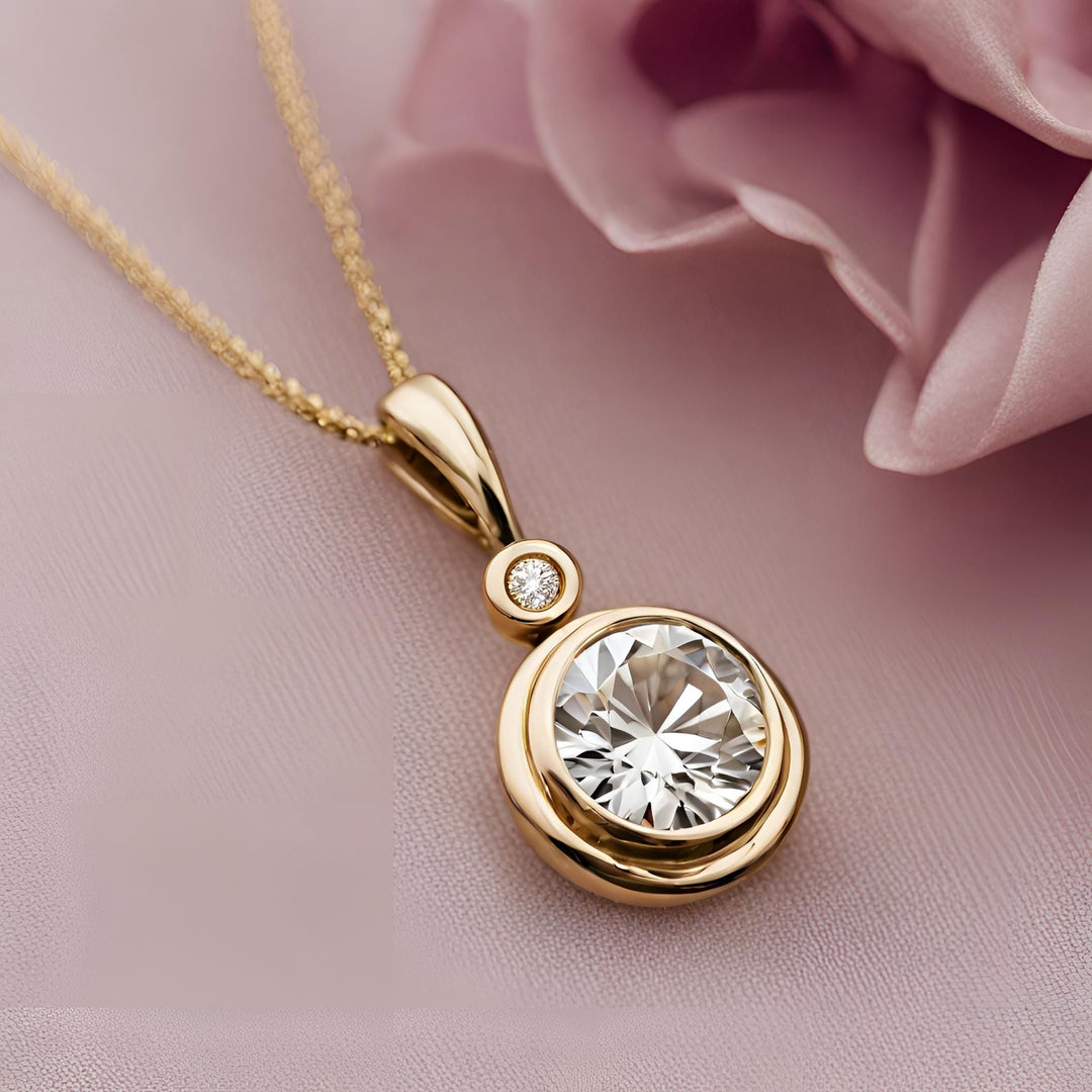 A round lab created diamond pendant in a 14K gold. This classic diamond necklace has two diamonds, one small and one large in gold bezel setting.
