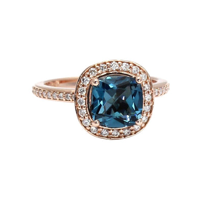 A cushion cut London Blue Topaz engagement ring with a diamond halo shown in rose gold from Rare Earth Jewelry.