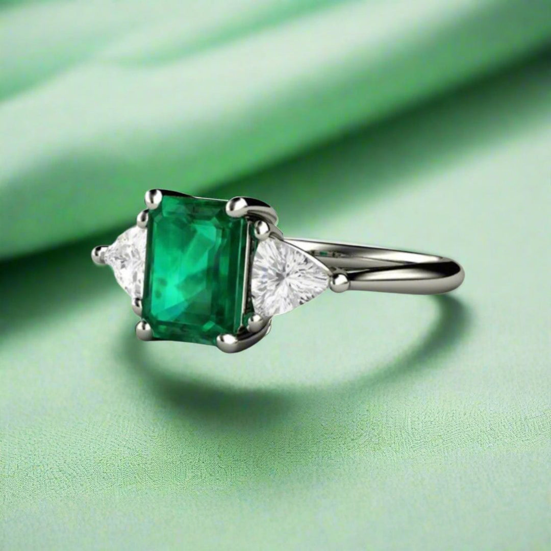 An emerald cut green emerald ring with white sapphire trillions in a 3 stone style setting, May birthstone engagement ring.