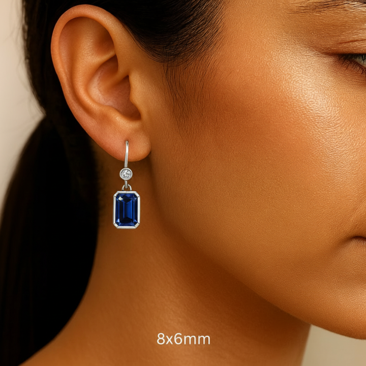8x6mm Emerald Cut Blue Sapphire Earrings with Diamonds shown on the Ear, Bezel Set Sapphire Dangle Earrings on French Ear Wires in 14K or 18K Gold and Platinum | Rare Earth Jewelry