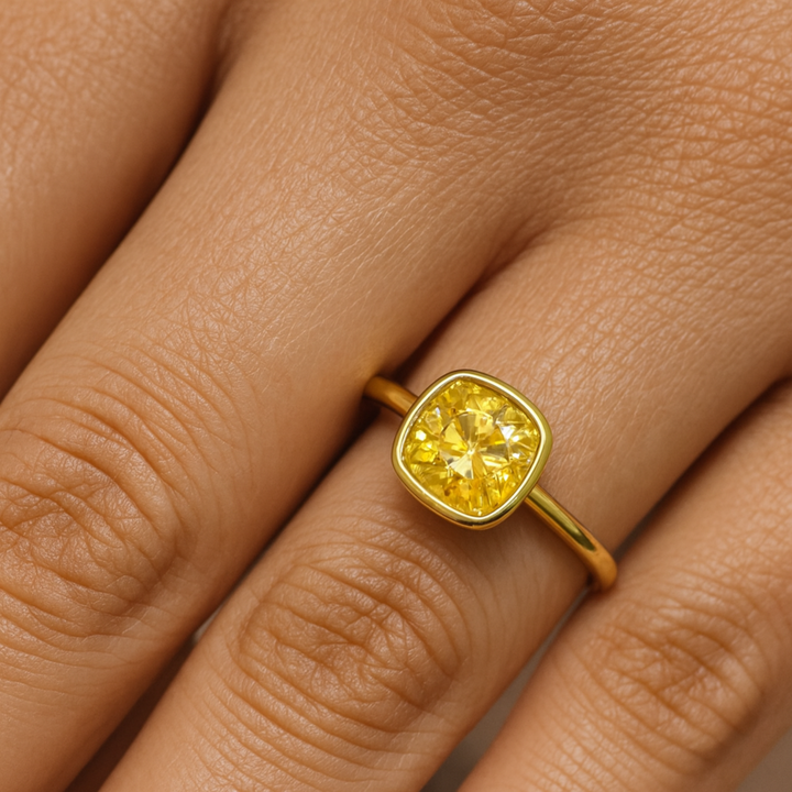 Cushion Cut Yellow Moissanite Engagement Ring Shown on the Finger, Simple Bezel Set Solitaire Yellow Diamond Alternative in Minimalist Design | Rare Earth Jewelry