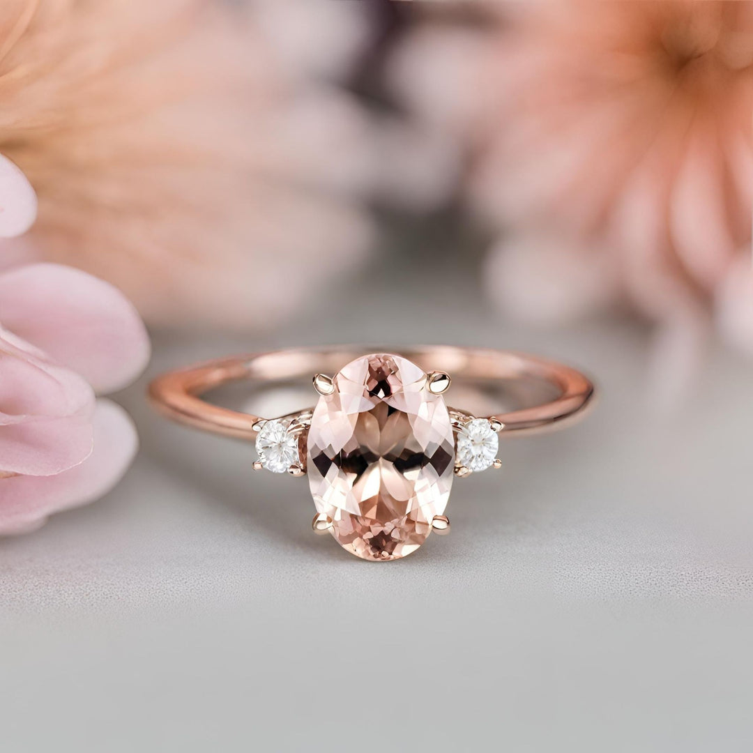 An oval natural morganite engagement ring in a classic 3 stone trio style setting with diamonds in rose gold from Rare Earth Jewelry.