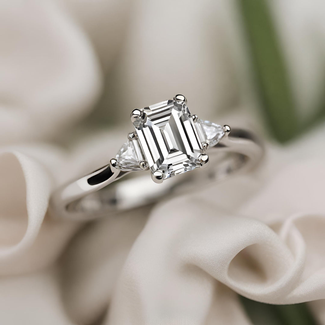 An emerald cut diamond engagement ring with a 3 stone design and diamond triangles in gold or platinum from Rare Earth Jewelry.