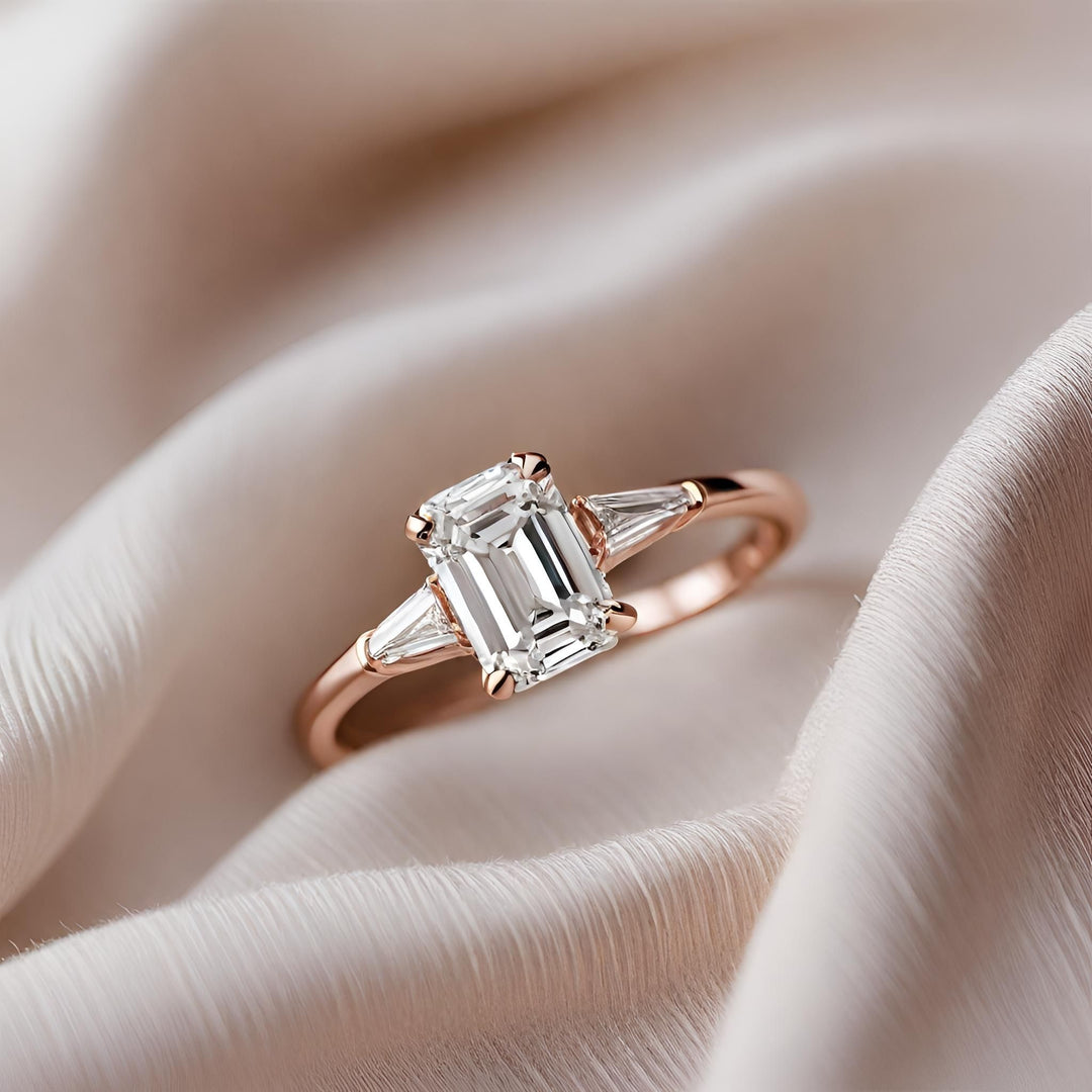 An emerald cut diamond engagement ring in a classic 3 stone style with tapered diamond baguettes in rose gold from Rare Earth Jewelry.