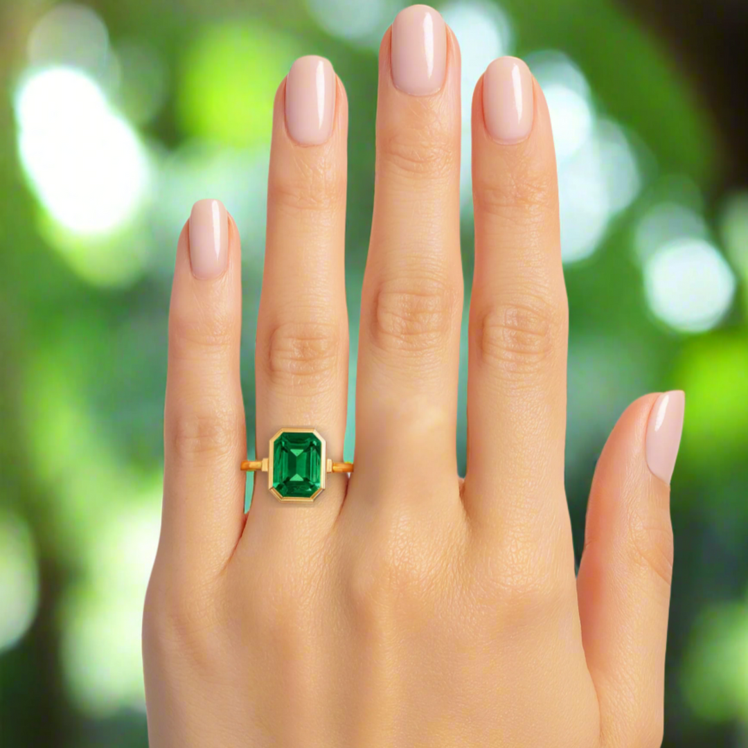 An emerald engagement ring with a 2 carat lab grown emerald bezel set into a modern, minimalist design.  A 9x7mm emerald cut emerald ring shown on the hand.  Rare Earth Jewelry
