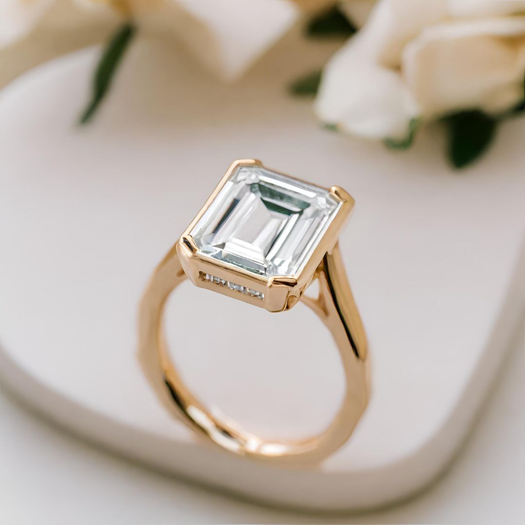 An emerald cut lab created diamond engagement ring in a half bezel solitaire design with wide prongs from Rare Earth Jewelry.