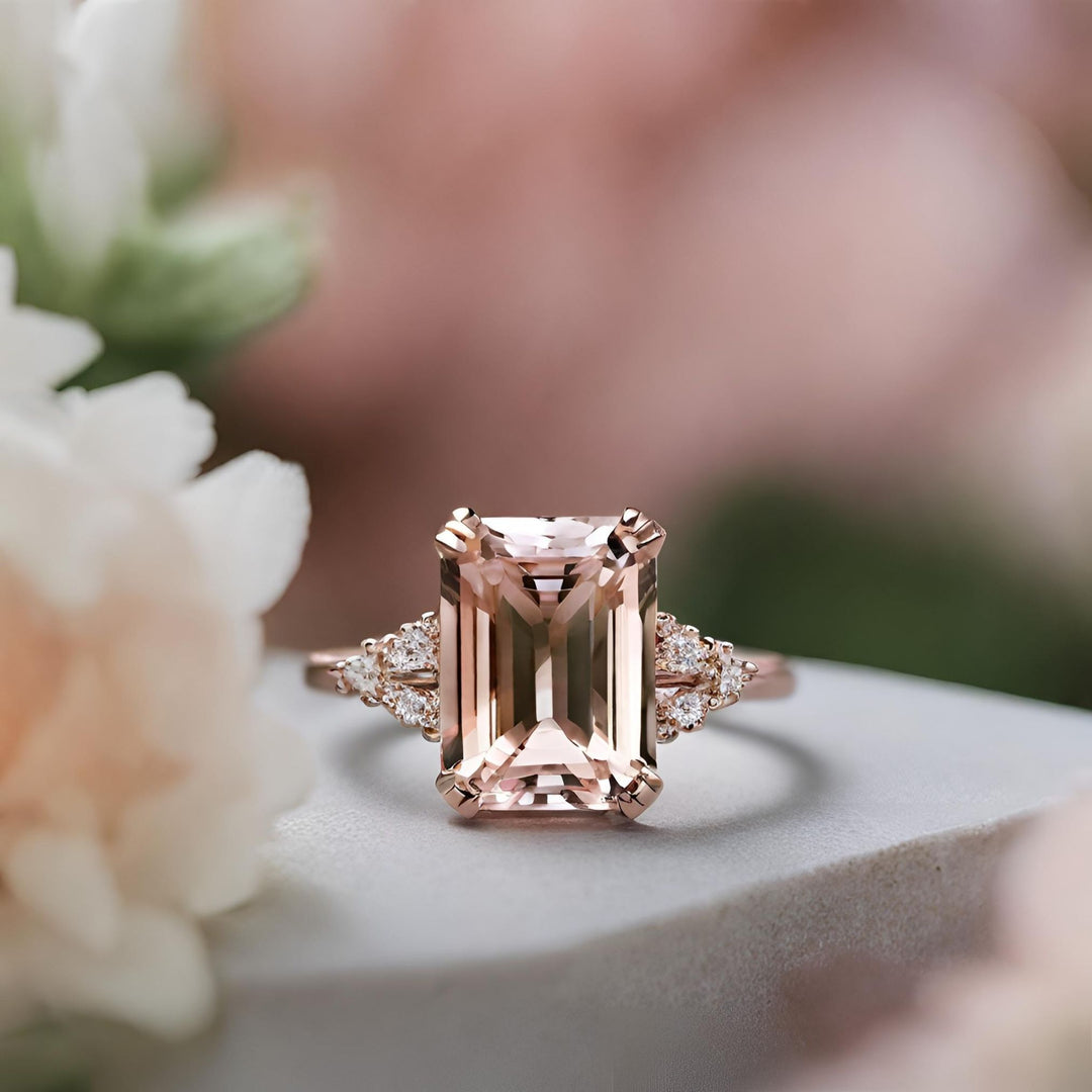 An emerald cut Morganite solitaire engagement ring with triple prongs and diamond accents in rose gold from Rare Earth Jewelry.