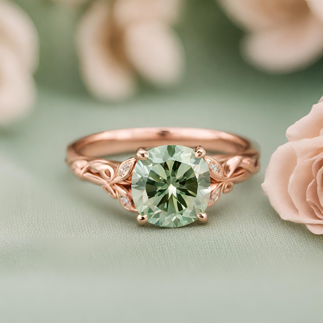 A round light green moissanite engagement ring in rose gold with a pretty leaf and branch design from Rare Earth Jewelry.