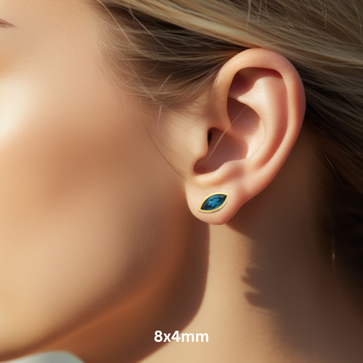 Close Up of London Blue Topaz Stud Earrings in a 8x4mm Marquise Cut on the Ear, 14K Yellow Gold Bezel Set Blue Gemstone Studs for Men or Women.  December birthstone earrings available as single earring or in pairs. | Rare Earth Jewelry