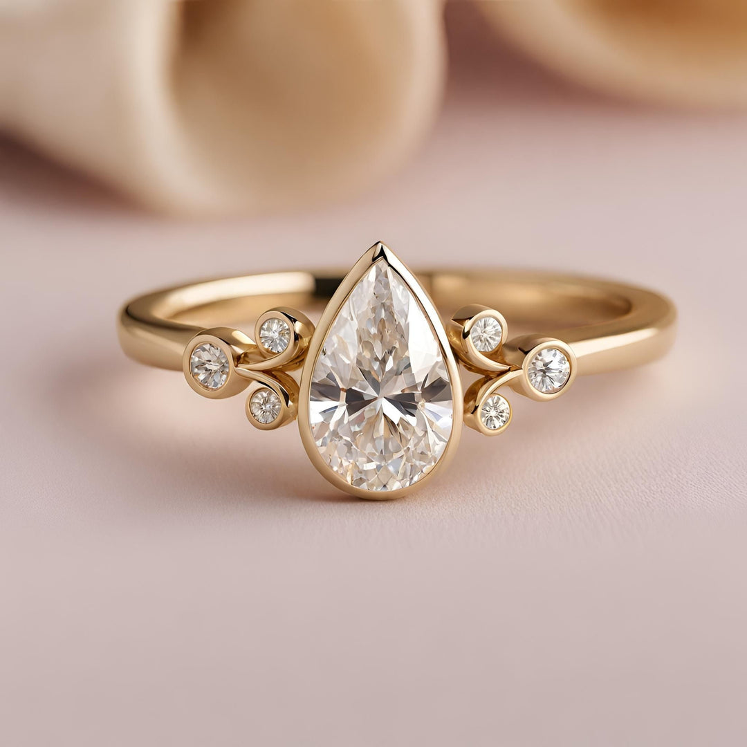 A pear cut diamond engagement ring in a bezel setting with fleur de lis details in 14K Gold from Rare Earth Jewelry.