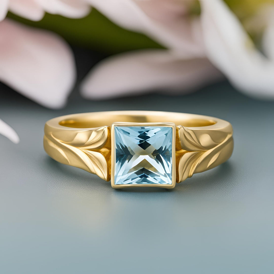 A princess cut Aquamarine ring in a modern bezel setting with a leaf design in matte finished yellow gold from Rare Earth Jewelry.