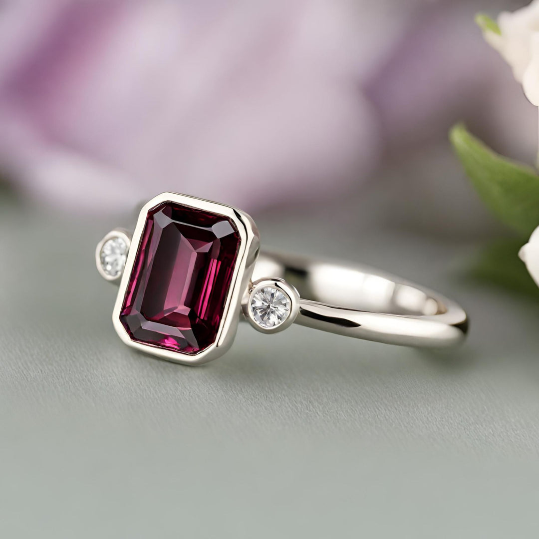 A red Rhodolite Garnet engagement ring in a modern emerald cut 3 stone style bezel setting from Rare Earth Jewelry.