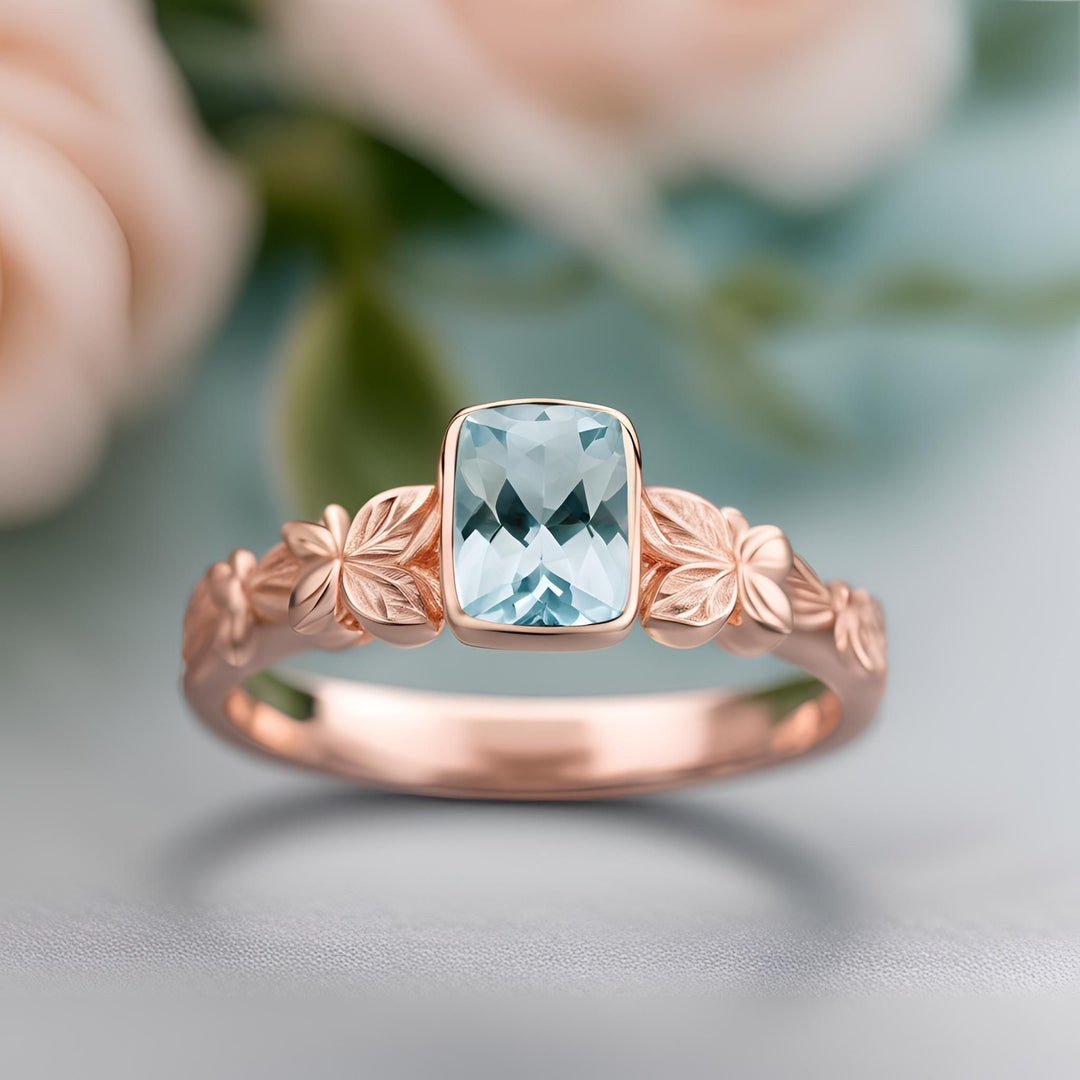 A bezel set cushion cut aquamarine ring with a flower and butterfly design in rose gold from Rare Earth Jewelry.