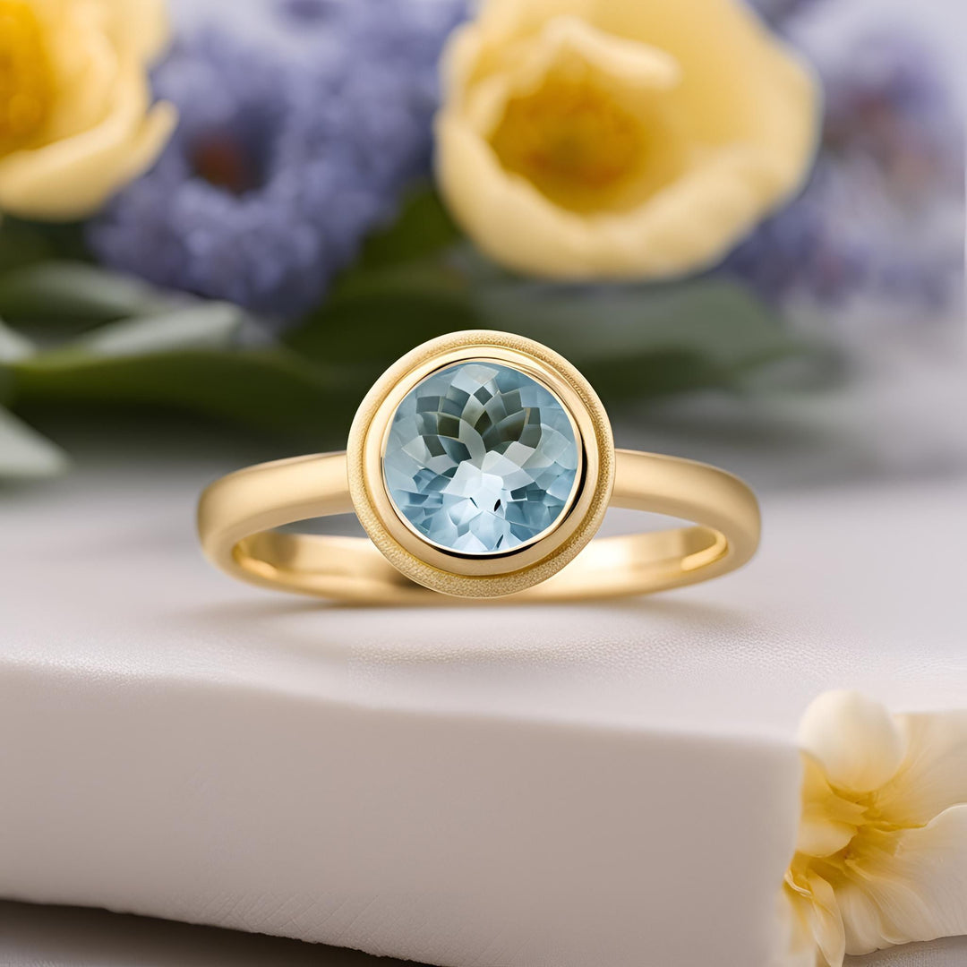 A round aquamarine engagement ring in a simple minimalist bezel setting on matte finish 18K Gold from Rare Earth Jewelry.