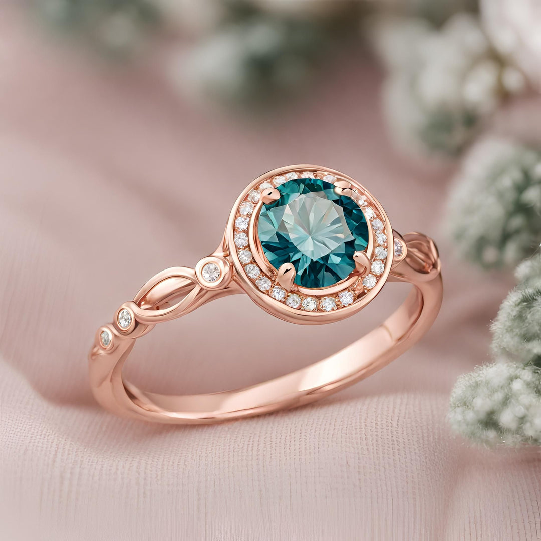 A round teal blue moissanite engagement ring with a vintage style halo design in rose gold from Rare Earth Jewelry.