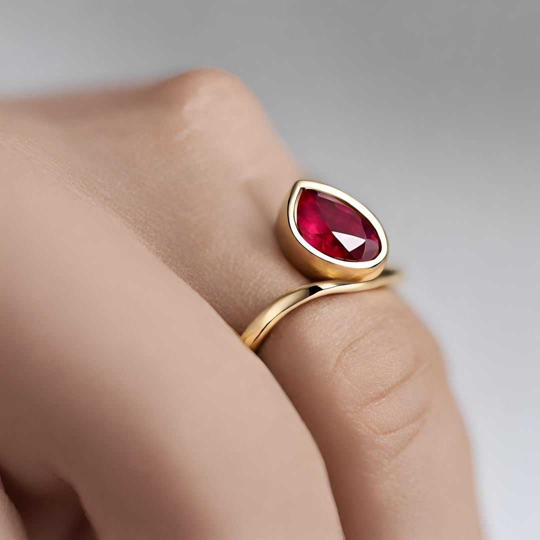 A pear cut bezel set ruby ring in a contemporary inverted design in yellow gold from Rare Earth Jewelry.