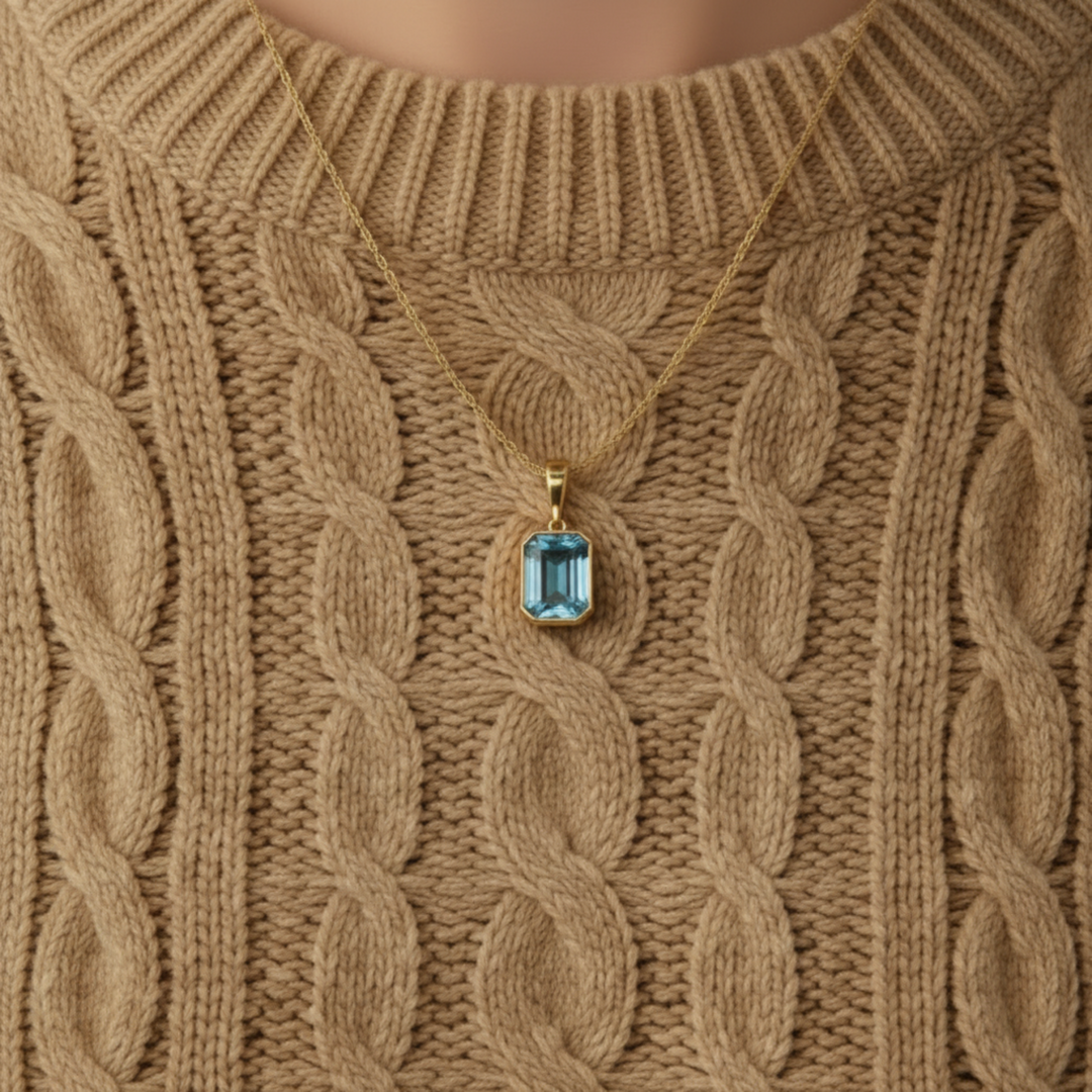 close up of natural sky blue topaz necklace emerald cut light blue stone pendant in 14k yellow gold worn with sweater | Rare Earth Jewelry
