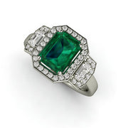 Three stone emerald and diamond engagement ring in an emerald cut halo design.
