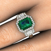 Three stone emerald ring on the finger.  Emerald cut diamond halo 3 stone ring on the hand.