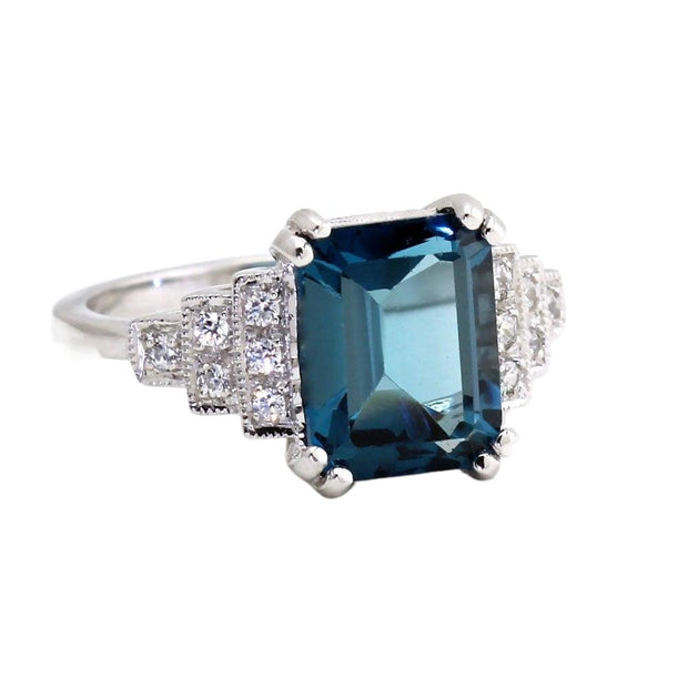 A vintage style London Blue Topaz ring with an Art Deco design, a 10x8mm Emerald Cut London Blue Topaz and Diamonds with milgrain detailing from Rare Earth Jewelry.