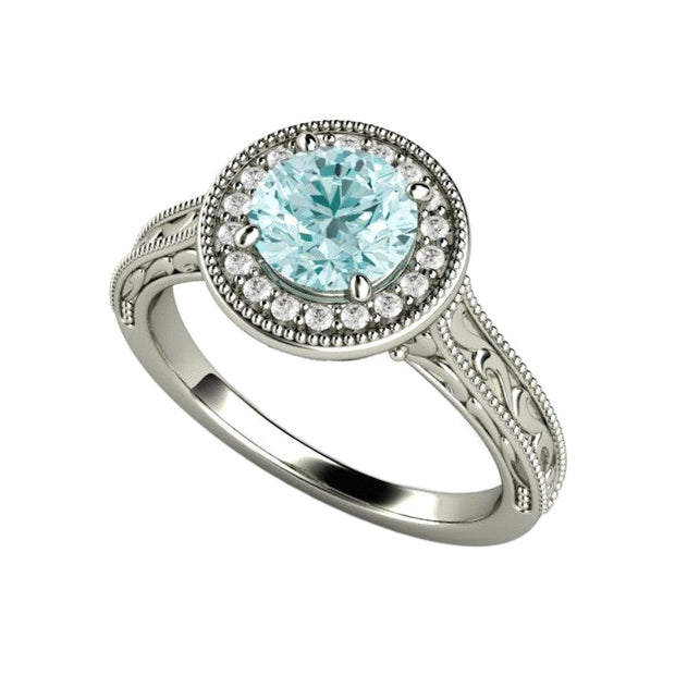 A vintage inspired Moissanite engagement ring with an engraved pattern and a diamond halo around a pretty pastel blue Moissanite from Rare Earth Jewelry.