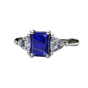 An emerald cut Blue Sapphire engagement ring in a three stone style with diamond trillions in gold or platinum.