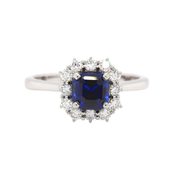 A Blue Sapphire engagement ring with a 1 carat asscher cut lab grown blue sapphire surrounded by a halo of natural diamonds in a vintage inspired cluster design.