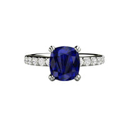 A cushion cut blue sapphire ring in a solitaire engagement ring setting with double prongs and pave set diamond accents in gold or platinum.