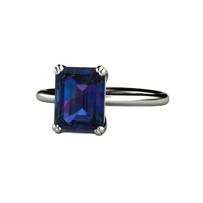 An emerald cut Alexandrite ring with a 2.75ct 9x7mm lab created Alexandrite in a solitaire style engagement ring with double prongs.  This unique color-change gemstone changes color in different lights and is available in gold or Platinum.