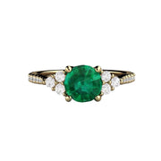 A round emerald engagement ring with a cluster of three diamonds on each side of the round emerald center and french pave set diamonds in the band, a unique and feminine design in gold or platinum from Rare Earth Jewelry.