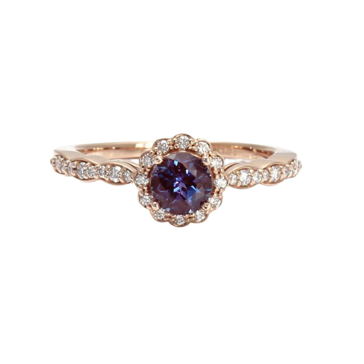 A unique engagement ring featuring Alexandrite, a gemstone that changes color!  Shown here in Rose Gold with a vintage style halo and shank with a scalloped design and diamond accents.