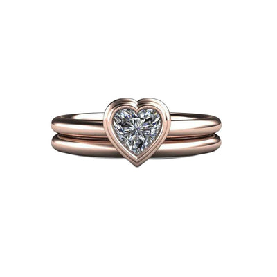 A bezel set heart cut Moissanite solitaire engagement ring and matching wedding band in rose gold from Rare Earth Jewelry.