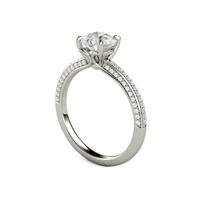 A 1 carat Forever One Moissanite solitaire engagement ring with pave set diamonds and claw shaped prongs in a dainty, feminine style from Rare Earth Jewelry.