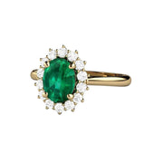 Feminine Emerald engagement ring with a 1.15ct oval cut green Emerald and a halo of natural diamonds. Classic vintage-style cluster setting in Gold or Platinum.