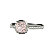 A cushion cut light pink sapphire engagement ring in a simple bezel setting with diamond accents in the band in gold or platinum from Rare Earth Jewelry.