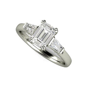 An emerald cut diamond engagement ring with a three stone design, tapered diamond baguettes and double prongs available in gold or platinum from Rare Earth Jewelry.
