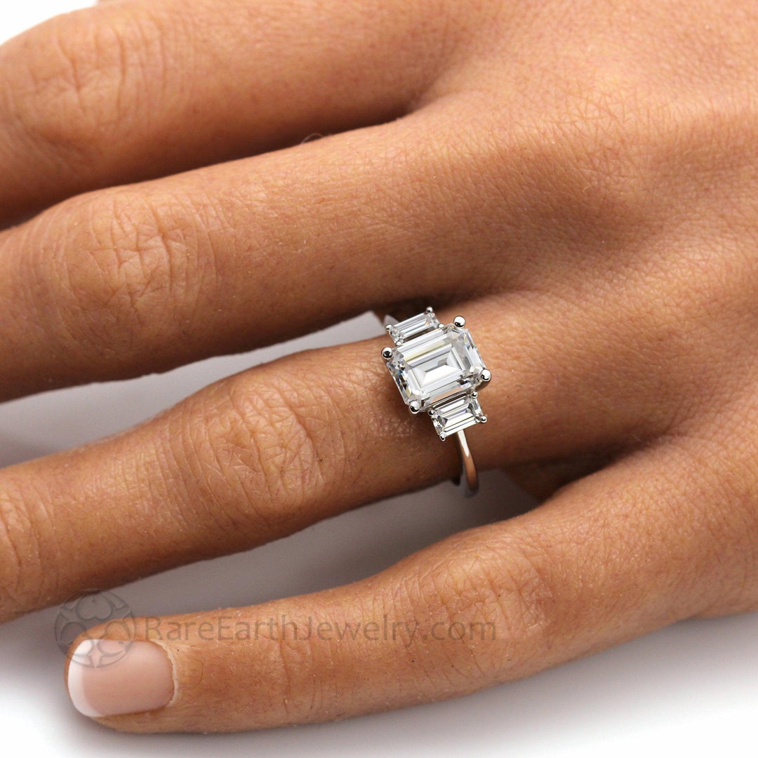 Three Stone Emerald Cut Moissanite Engagement Ring on Hand, Lab Created Diamond Alternative Engagement Rings | Rare Earth Jewelry