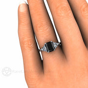 Natural Black Diamond Engagement Ring on the Finger, three stone style with diamond trillions from Rare Earth Jewelry